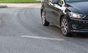 Schwarzes Auto fährt um eine Kurve, Reifen quietschen.