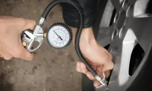Person korrigiert den Reifendruck mit einem Manometer.