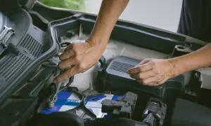 Hände wechseln eine Autobatterie. Ein Schraubenschlüssel löst die Klemmen. Start stop batterie wechseln ohne anlernen ist hier möglich.