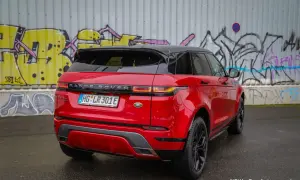Ein glänzender, **range rover rot** steht vor einer Graffiti-Wand. Das Auto hat ein schwarzes Dach und schwarze Felgen.