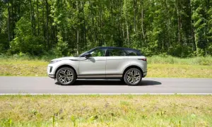Ein silberner Range Rover Evoque fährt auf einer Straße durch einen grünen Wald.