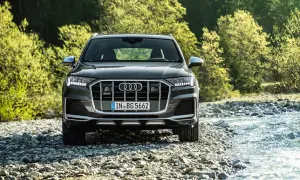Ein dunkler Audi SQ8 PS steht am Ufer eines steinigen Flusses, umgeben von üppigem Grün.