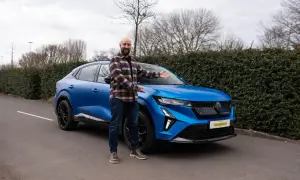 Ein Mann präsentiert stolz den neuen, blauen Renault Rafale vor einer Hecke.