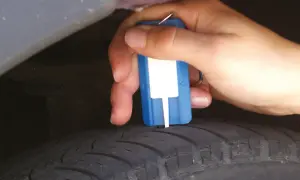 Hand misst Profiltiefe eines Reifens mit einem Messgerät. So prüfen Sie, wie alt Winterreifen sind.