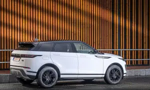 Weißer Range Rover Evoque Benziner mit schwarzem Dach parkt vor einer Holzwand.