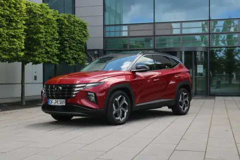 Roter Hyundai Tucson 2026 vor einem modernen Gebäude mit Bäumen.