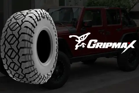 Ein grobstolliger Reifen von Gripmax neben einem roten Jeep. Perfekt für jedes Abenteuer.