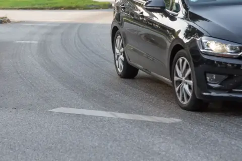 Schwarzes Auto fährt um eine Kurve, Reifen quietschen.
