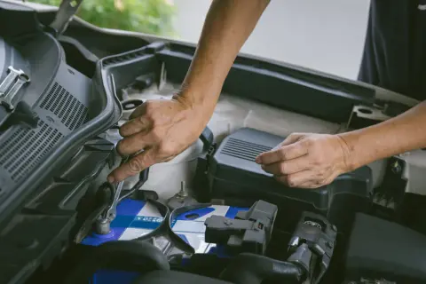 Hände wechseln eine Autobatterie. Ein Schraubenschlüssel löst die Klemmen. Start stop batterie wechseln ohne anlernen ist hier möglich.