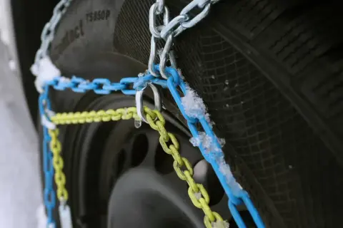 Schneeketten in Blau und Gelb sind an einem Reifen montiert, bereit für den Einsatz bei Schnee und Eis. Allradfahrzeuge profitieren besonders von dieser Traktionshilfe.