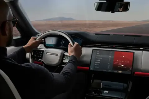 Mann fährt Range Rover, steuert über das intuitive Land Rover InControl System. Die Ambientebeleuchtung "Dynamic Red" leuchtet.