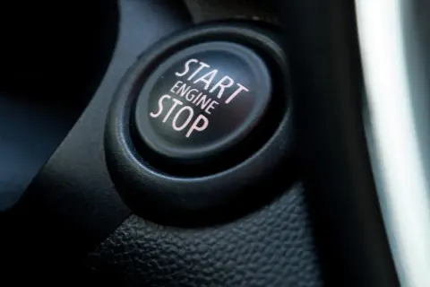 Nahaufnahme eines Start/Stop-Knopfes im Auto. Der Knopf ist schwarz mit rosa Schrift.
