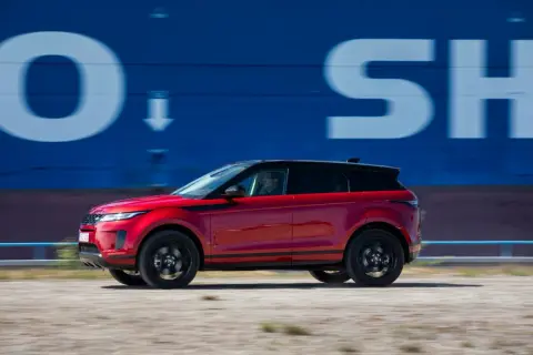 Roter Range Rover Evoque 2022 fährt an blauer Wand mit weißen Buchstaben vorbei.