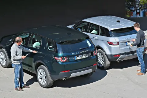 Zwei Männer inspizieren zwei Land Rover: einen dunklen Discovery Sport und einen silbernen Range Rover Evoque. Ein kleiner Land Rover, der Discovery Sport, steht im Vordergrund.