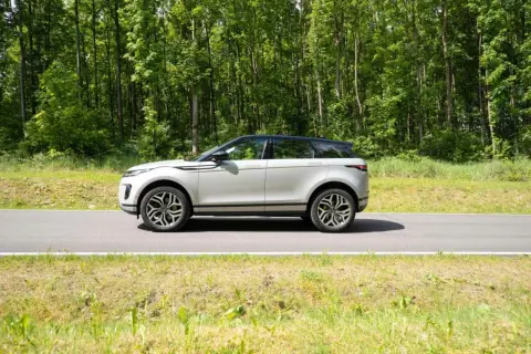 Ein silberner Range Rover Evoque fährt auf einer Straße durch einen grünen Wald.