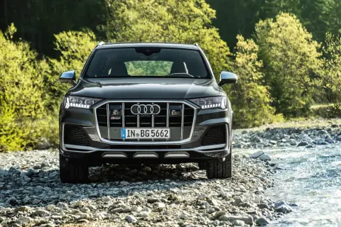 Ein dunkler Audi SQ8 PS steht am Ufer eines steinigen Flusses, umgeben von üppigem Grün.