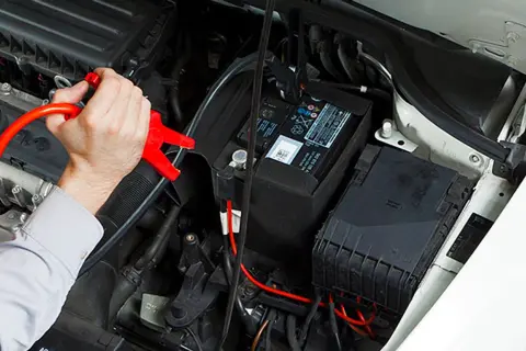 Hand hält rote Starthilfeklemme, die an der Autobatterie befestigt wird. Dies ist die zweite Batterie im Auto, die zum Starten benötigt wird.