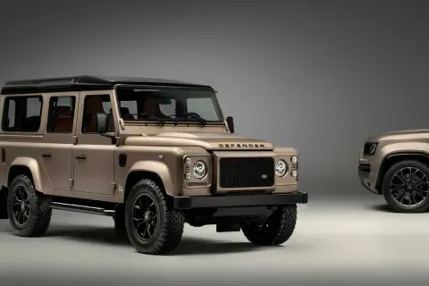 Zwei bronzefarbene Land Rover Defender stehen nebeneinander. Der vordere, klassische Defender ist bereit, wenn Sie einen Land Rover kaufen möchten.