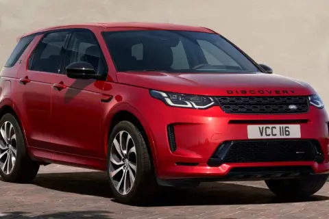 Roter Range Rover Discovery Sport, ein **range rover approved** Fahrzeug, parkt vor einer hellen Wand mit grünen Fensterläden.