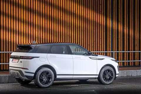 Weißer Range Rover Evoque Benziner mit schwarzem Dach parkt vor einer Holzwand.
