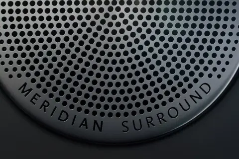 Nahaufnahme eines Lautsprechergitters mit der Aufschrift "MERIDIAN SURROUND". Gute Meridian Soundsystem Erfahrungen sind garantiert.