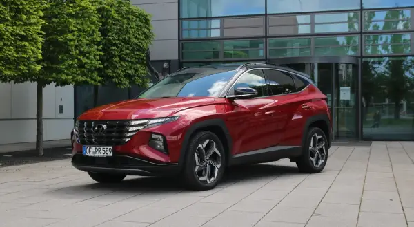 Roter Hyundai Tucson 2026 vor einem modernen Gebäude mit Bäumen.