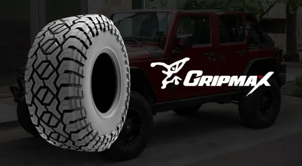 Ein grobstolliger Reifen von Gripmax neben einem roten Jeep. Perfekt für jedes Abenteuer.