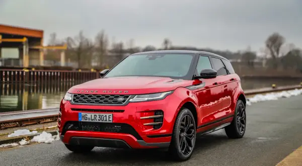 Roter Range Rover Evoque parkt am Wasser. Die Anhängelast ist für Abenteuer bereit.