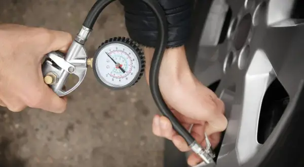 Person korrigiert den Reifendruck mit einem Manometer.