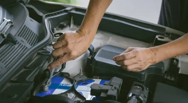 Hände wechseln eine Autobatterie. Ein Schraubenschlüssel löst die Klemmen. Start stop batterie wechseln ohne anlernen ist hier möglich.