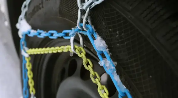 Schneeketten in Blau und Gelb sind an einem Reifen montiert, bereit für den Einsatz bei Schnee und Eis. Allradfahrzeuge profitieren besonders von dieser Traktionshilfe.