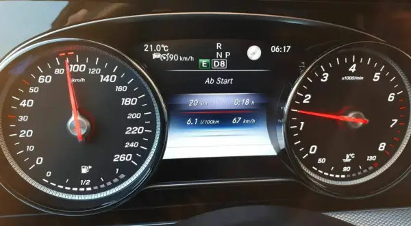 Fahrzeug-Display eines Mercedes mit Tacho bei 90 km/h, Verbrauchsanzeige und aktiver Tempomat-Funktion.