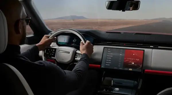 Mann fährt Range Rover, steuert über das intuitive Land Rover InControl System. Die Ambientebeleuchtung "Dynamic Red" leuchtet.