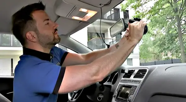 Mann montiert eine Dashcam im Auto. So kann er seine Fahrten aufzeichnen und sein Fahrzeug nachrüsten.