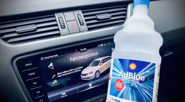 Flasche AdBlue neben dem Armaturenbrett. Fahrzeugstatus zeigt "Bitte AdBlue nachfüllen. Kein Motorstart in 300 km.