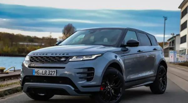 Grauer Range Rover Evoque, dessen Länge durch die dynamische Seitenansicht betont wird. Ein stilvolles SUV am Wasser.