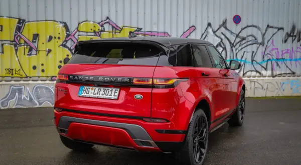 Ein glänzender, **range rover rot** steht vor einer Graffiti-Wand. Das Auto hat ein schwarzes Dach und schwarze Felgen.