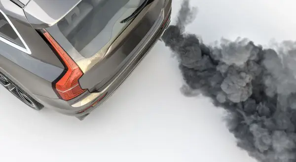 Graues Auto stößt dichten, schwarzen Rauch aus dem Auspuff aus.