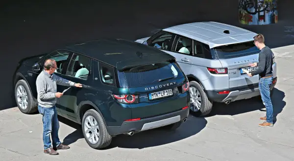 Zwei Männer inspizieren zwei Land Rover: einen dunklen Discovery Sport und einen silbernen Range Rover Evoque. Ein kleiner Land Rover, der Discovery Sport, steht im Vordergrund.