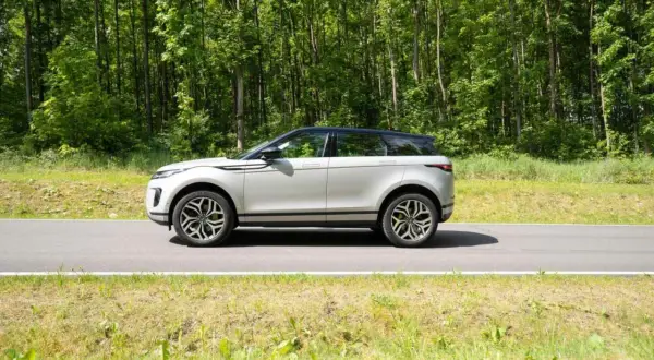 Ein silberner Range Rover Evoque fährt auf einer Straße durch einen grünen Wald.