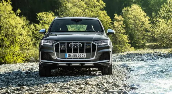 Ein dunkler Audi SQ8 PS steht am Ufer eines steinigen Flusses, umgeben von üppigem Grün.