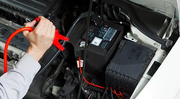 Hand hält rote Starthilfeklemme, die an der Autobatterie befestigt wird. Dies ist die zweite Batterie im Auto, die zum Starten benötigt wird.