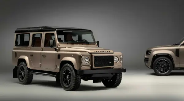 Zwei bronzefarbene Land Rover Defender stehen nebeneinander. Der vordere, klassische Defender ist bereit, wenn Sie einen Land Rover kaufen möchten.