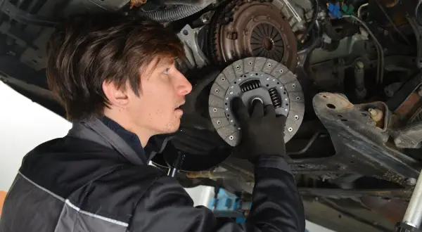 Mechaniker hält neue Kupplungsscheibe. Die Kosten für den Kupplung wechseln sind oft eine Überraschung.