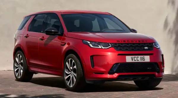 Roter Range Rover Discovery Sport, ein **range rover approved** Fahrzeug, parkt vor einer hellen Wand mit grünen Fensterläden.