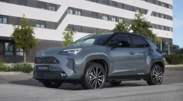 Grauer Toyota Yaris Cross 2026 mit GR-Sport-Akzenten steht vor einem modernen Gebäude.