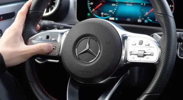 Hand stellt Mercedes Distronic ein. Lenkrad mit Bedienelementen und Stern-Logo.