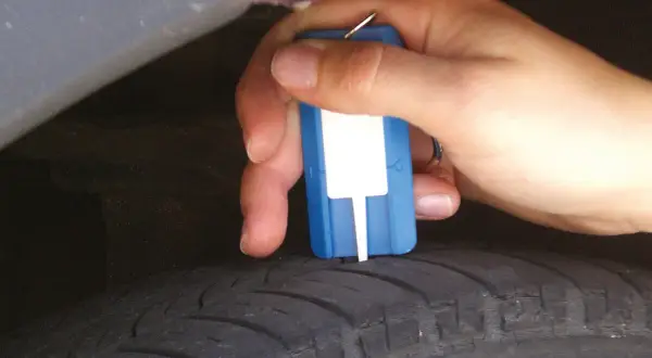 Hand misst Profiltiefe eines Reifens mit einem Messgerät. So prüfen Sie, wie alt Winterreifen sind.