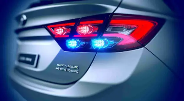 Rückansicht eines Autos mit leuchtenden roten Bremslichtern und blauen Akzentlichtern. Die dynamische Bremsleuchte sorgt für Sichtbarkeit.