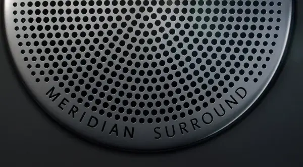 Nahaufnahme eines Lautsprechergitters mit der Aufschrift "MERIDIAN SURROUND". Gute Meridian Soundsystem Erfahrungen sind garantiert.